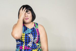 A person of size in a bright, colorful dress has their hand covering half their face with an exasperated expression.