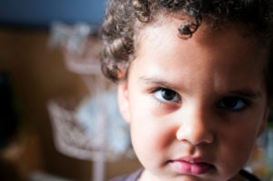 An angry child looks at the viewer; the background is out of focus.