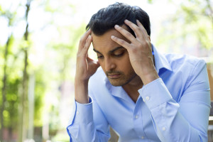 A stressed person has their hands on head, sitting outside.