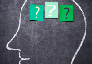 A human head is drawn on a chalkboard. In the brain are three slips of green paper with question marks on them.